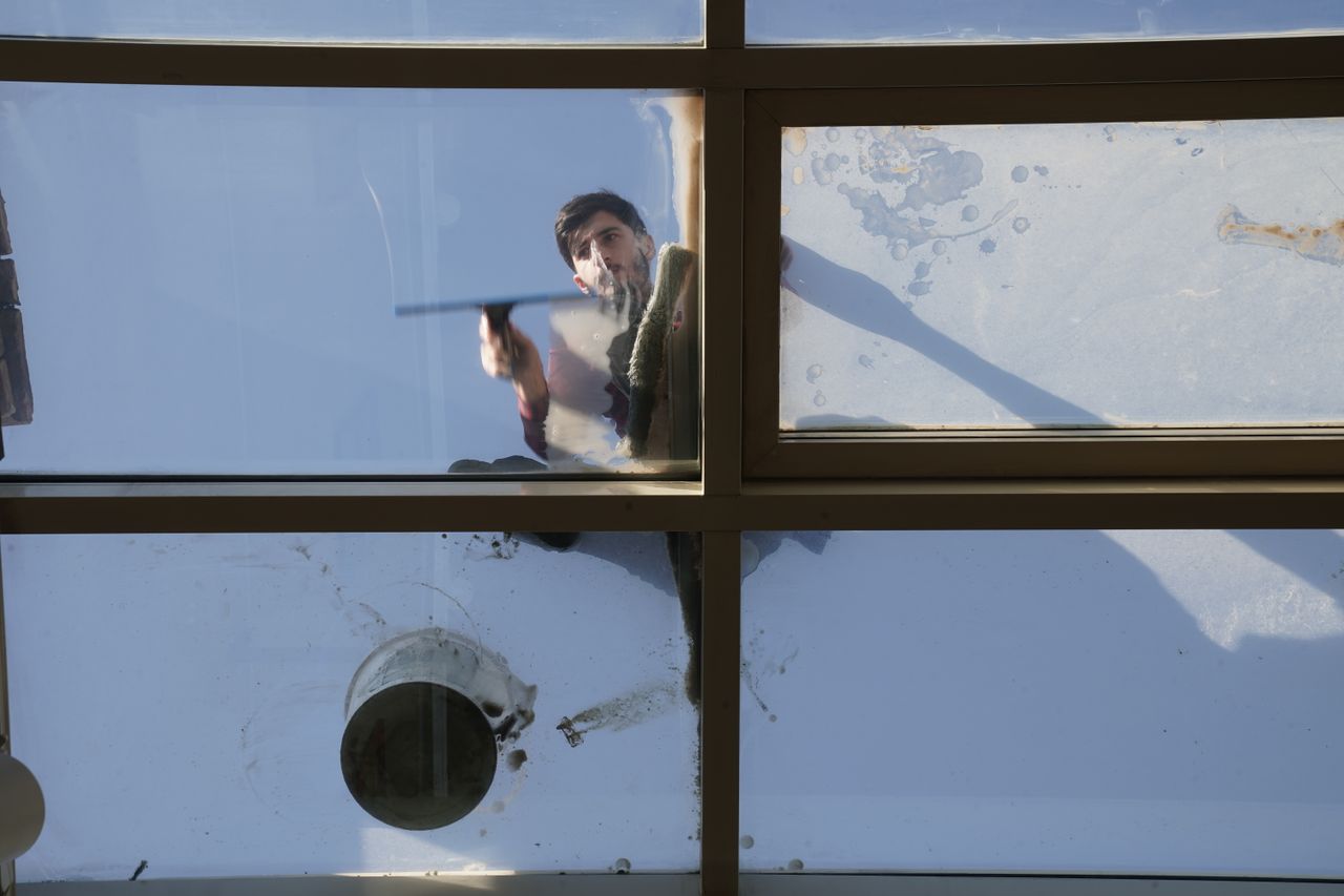 gallery-04 A male window cleaner washing the exterior glass roof from above with a tool during daylight.