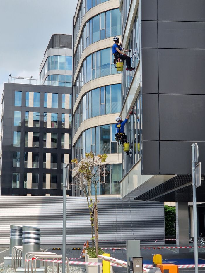 gallery-05 Two workers clean windows on a tall office building in a city setting.