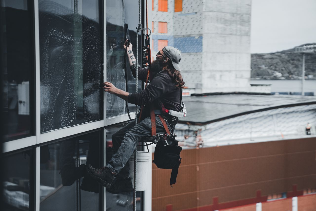 home-img A man cleaning skyscraper windows with a harness, showcasing urban high-rise work.